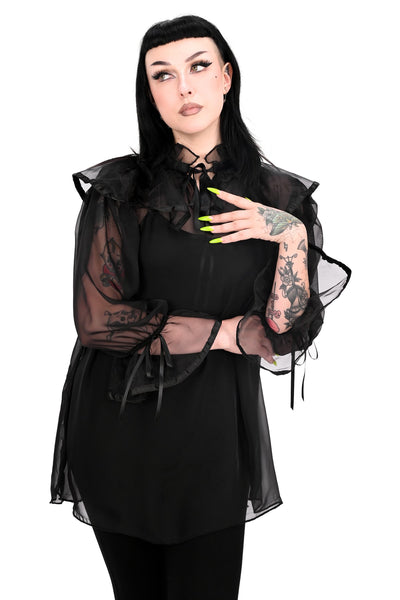 A model wearing a black chiffon sheer tunic with ruffled keyhole detail collar and 3/4 sleeves with gathered ruffled cuffs, both with black satin trim and adjustable ties. Shown from front styled with black bodysuit