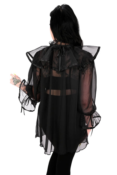 A model wearing a black chiffon sheer tunic with ruffled keyhole detail collar and 3/4 sleeves with gathered ruffled cuffs, both with black satin trim and adjustable ties. Shown from back styled with black bodysuit