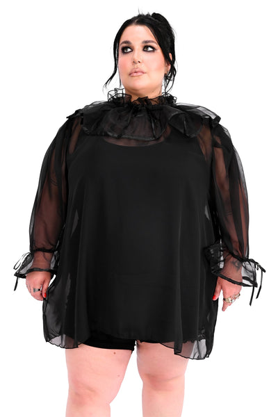 A plus size model wearing a black chiffon sheer tunic with ruffled keyhole detail collar and 3/4 sleeves with gathered ruffled cuffs, both with black satin trim and adjustable ties. Shown from front styled with black leotard 