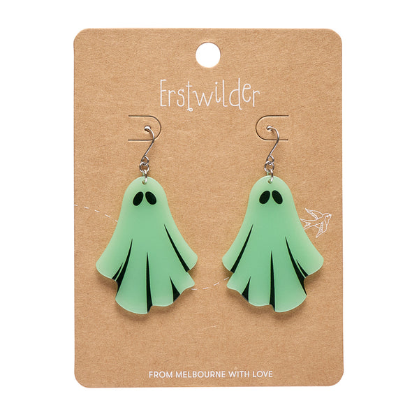 A pair of mint green ghost-shaped dangle earrings with black eyes and folds, displayed on a brown kraft paper card by Erstwilder.