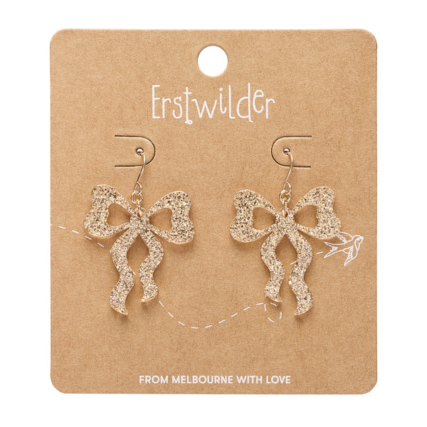 A pair of glittery gold bow-shaped dangle earrings on a brown kraft paper display card. The card features the brand name 'Erstwilder' printed at the top and the phrase 'FROM MELBOURNE WITH LOVE' at the bottom.