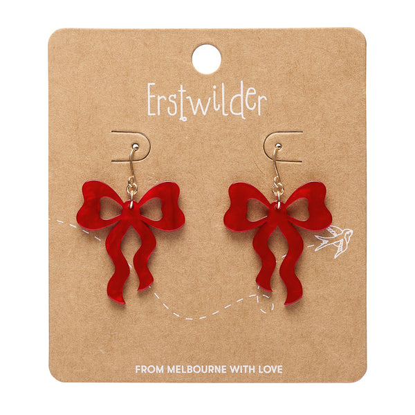 A pair of red bow-shaped dangle earrings displayed on a brown kraft paper card. The card has the brand name 'Erstwilder' printed at the top and the text 'FROM MELBOURNE WITH LOVE' at the bottom.