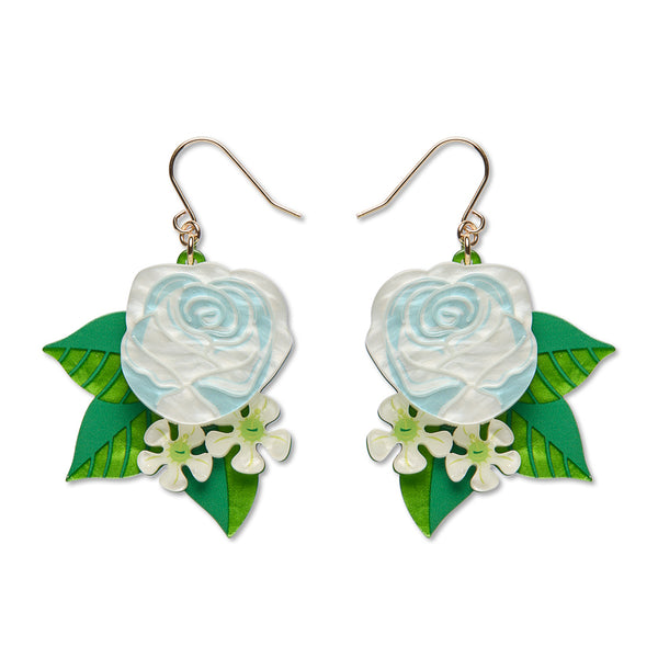 A pair of dangling earrings featuring light blue and white rose charms, green leaf accents, and small white flowers, suspended from gold-tone hooks against a plain white background.