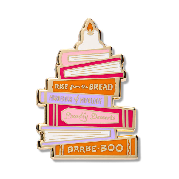 A novelty enamel pin shaped like a stack of books, styled as a birthday cake with gold metal outlines and colorful book spines in pink, orange, purple, and white. The books feature text such as 'RISE from the BREAD', 'MURDEROUS MIXOLOGY', 'Deadly Desserts', and 'BARBE-BOO'.