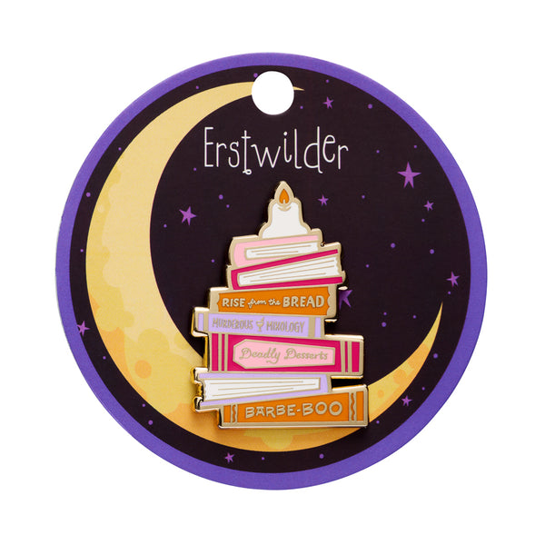 A novelty enamel pin shaped like a stack of books, styled as a birthday cake with gold metal outlines and colorful book spines in pink, orange, purple, and white. The books feature text such as 'RISE from the BREAD', 'MURDEROUS MIXOLOGY', 'Deadly Desserts', and 'BARBE-BOO'. shown on illustrated round backer card packaging