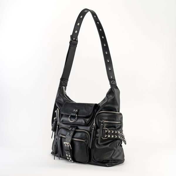 black textured faux leather crossbody bag with 8 exterior pockets with silver metal zip closure and cone stud & o-ring detail on oversized strap detail. Bag has 27" adjustable self strap. Shown from side