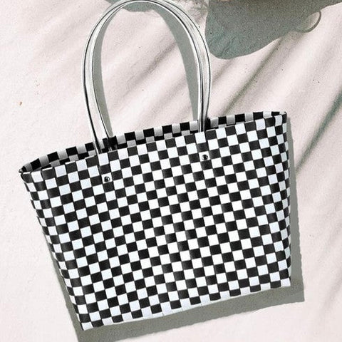 Black and white basket weave style plastic tote with clear plastic tube handle. Shown flat