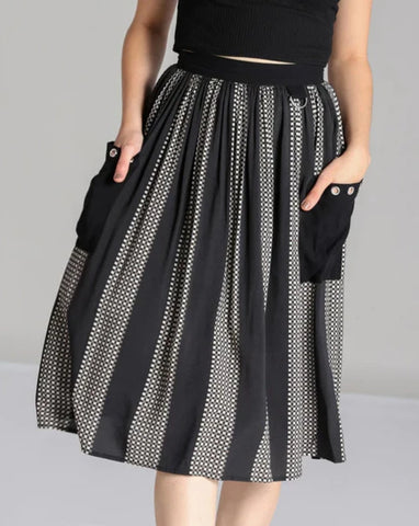 A model wearing a midi length skirt in a black and grey check plaid with alternating black vertical stripes. It has a self waistband with silver metal D-ring detail at the left hip and large black patch pockets with silver metal grommets at the hem of the pockets. Shown cropped close up from the front