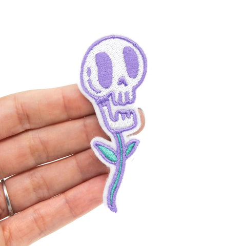 Embroidered felt patch of a white and purple skull with open mouth & purple and green stem and leaves