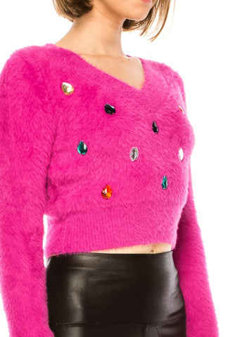 Model wearing a cropped v-neckline long sleeve faux mohair sweater in fuchsia. It has several multicolored oversized teardrop shaped jewels affixed to the front of the sweater. Shown from the front