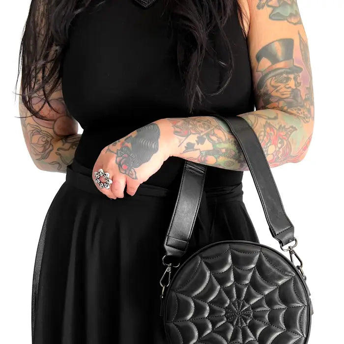 Model holding black faux leather round handbag with quilted spiderweb design