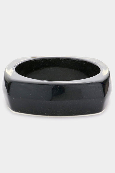 shiny square resin bangle with rounded sides in black with tiny flecks of silver and blue glitter and translucent top and bottom. Shown from side