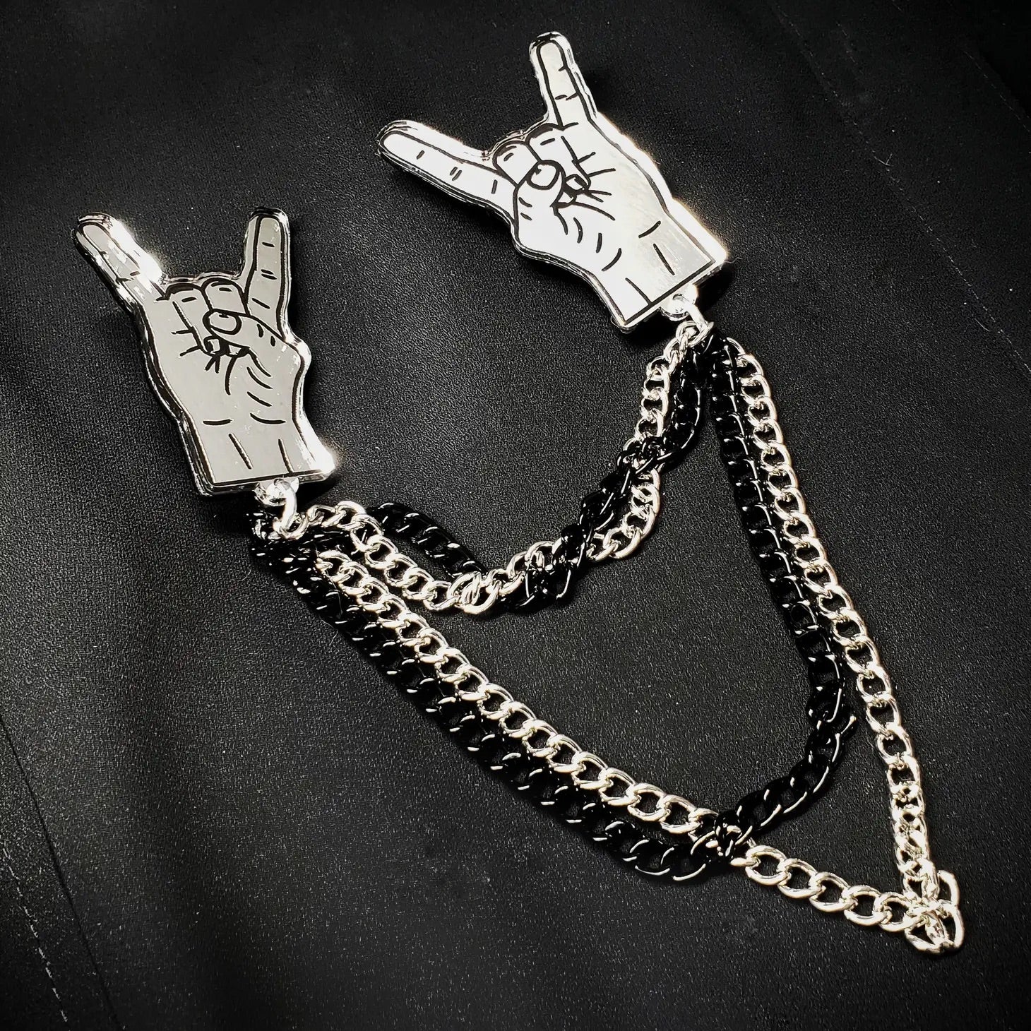 Laser cut silver mirrored acrylic hands throwing metal horns connected by 4 black and silver cable link chains. Shown laying flat