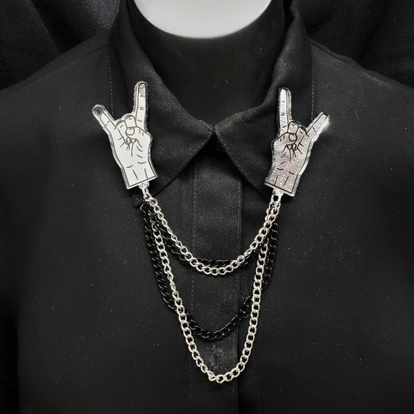 Laser cut silver mirrored acrylic hands throwing metal horns connected by 4 black and silver cable link chains. Shown on a black collared shirt