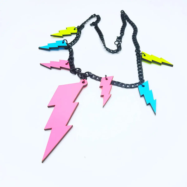 18” statement necklace made of black enameled curb chain decorated with 7 neon lightning bolts. 6 of the bolts are 1 1/2” tall and are yellow, blue, and pink, while one bolt at the center is 3 3/4” and pink 
