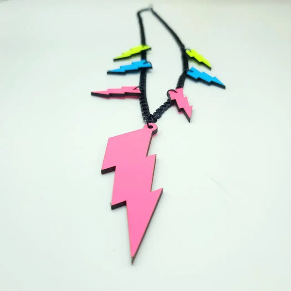 18” statement necklace made of black enameled curb chain decorated with 7 neon lightning bolts. 6 of the bolts are 1 1/2” tall and are yellow, blue, and pink, while one bolt at the center is 3 3/4” and pink