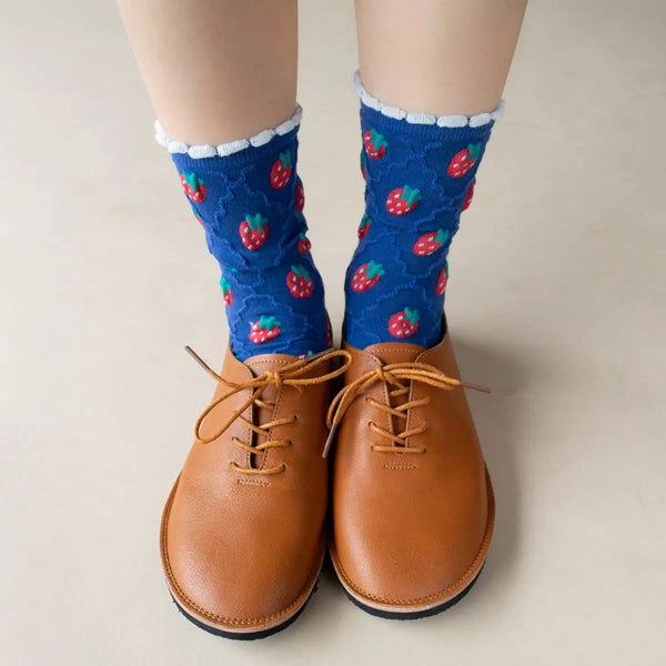 cotton knit socks in blue with a textured knit-in pattern of red strawberries and a matching wavy diamond pattern. Shown worn by a model wearing brown Oxford shoes