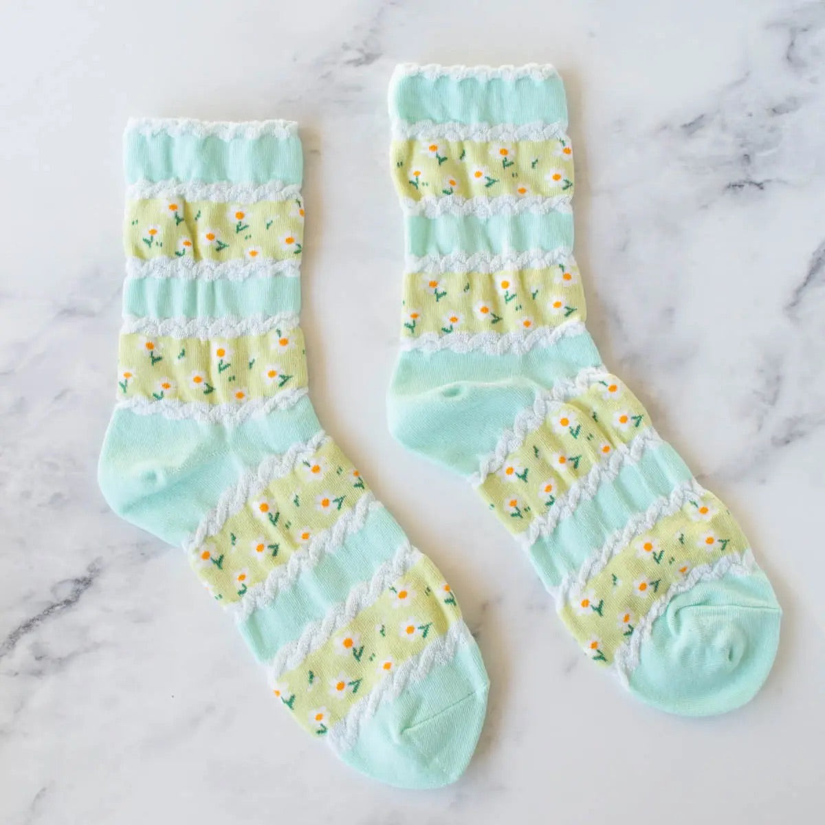 Cotton knit socks in a light minty green with a textured stripe pattern in an alternating shade of yellow-green with allover daisy knit-in pattern. Shown lying flat
