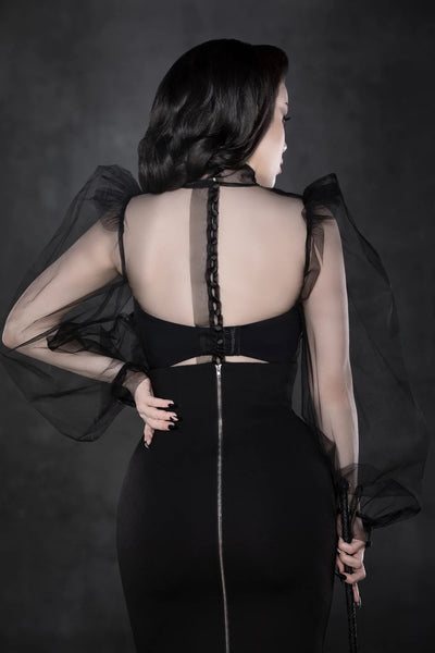 A model wearing a long sleeved blouse made of sheer lightweight black tulle. It has a banded neck, balloon style sleeves with puffed shoulders, black satin buttons running down the back of the blouse. Shown from the back.