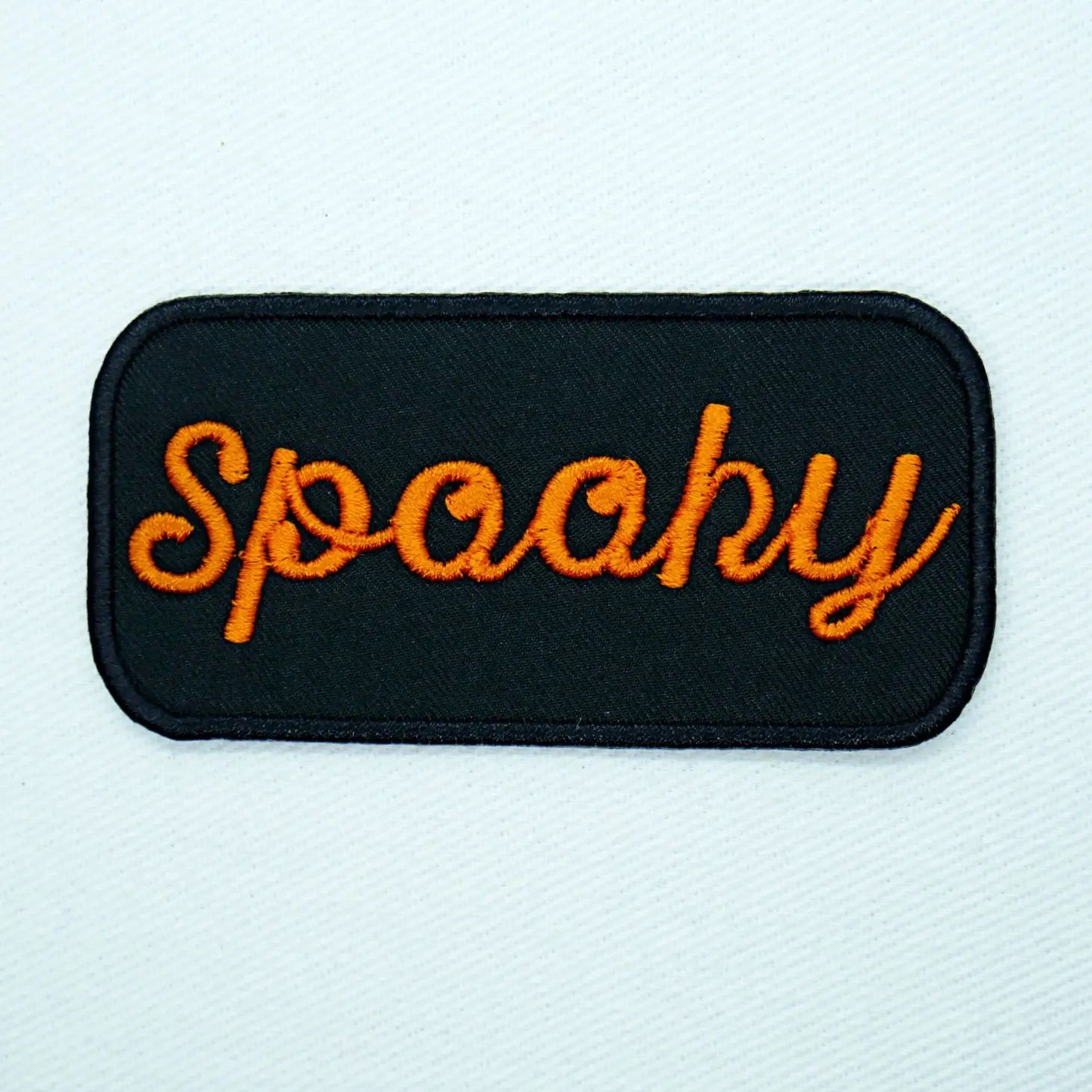 Black & orange "Spooky” cursive name tag style embroidered patch. Black background with orange fint