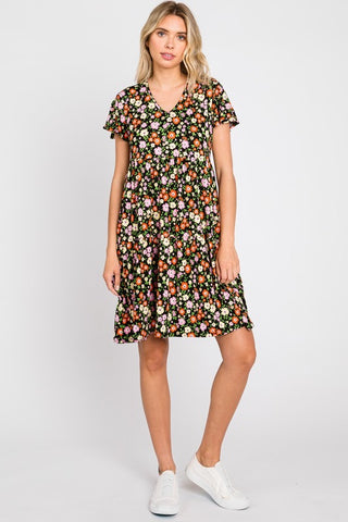 Knit dress in a red, pink, yellow, and green floral pattern on a black background. The dress has a shallow v-neck and short flutter sleeves with a gathered at the waist tiered skirt that ends just above the knee. Shown on a model 