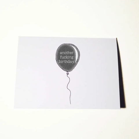 A greeting card with an image of a single black balloon on a string with the message “another fucking birthday”
