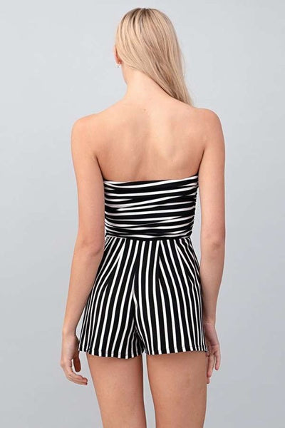 A model wearing a strapless black and white striped romper. It has slight ruching at the bodice and relaxed fit style high-waisted shorts. Seen from behind 