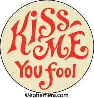 Vintage inspired “Kiss me you fool” 1.25" round metal pin-back button in red script on a beige background 