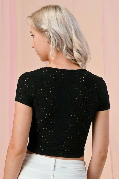 Black eyelet fabric crop top with square neckline, a lightly ruched bodice, and cap sleeves. Shown on a model from the back 