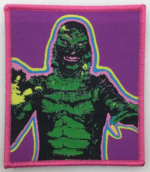 Rectangular patch of the Creature from the Black Lagoon surrounded by stripes of neon pink, blue, and yellow on a purple background with pink border