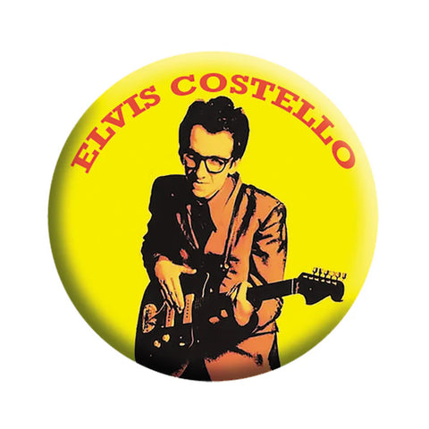 portrait of Elvis Costello in orange, red, and yellow circa his 1977 first album, My Aim Is True, on a 1.5” round metal button