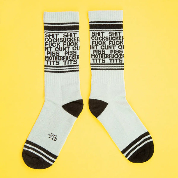 Unisex crew length cotton blend stretch gym socks with the words shit, cocksucker, fuck, cunt, piss, motherfucker, tits with black and grey stripes. Shown on yellow background 
