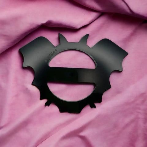 Shiny black bat shaped t-shirt slide buckle on a pink fabric background 