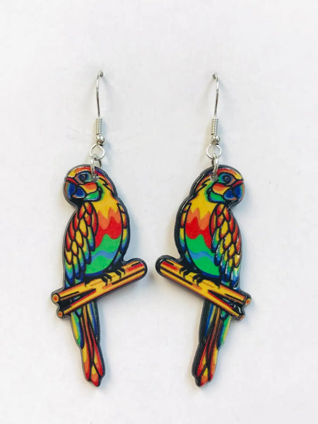 A bright green, blue, yellow, orange, and red parrot perched on a piece of wood as a pair of earrings. Printed image is mirrored on both sides and coated with acrylic resin
