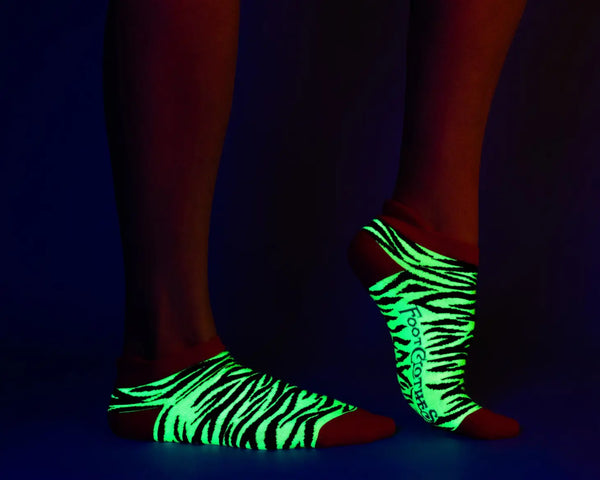 neon yellow and black zebra stripe pattern soft stretch cotton blend ankle socks with neon pink cuffs, heels, and toes. Shown under blacklight on a models feet
