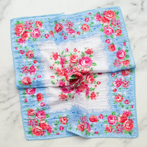 vintage handkerchief inspired cotton scarf in beige with a lush rose motif in red, pink and green with a matching border on a light blue background and finished with embroidered scallop trim