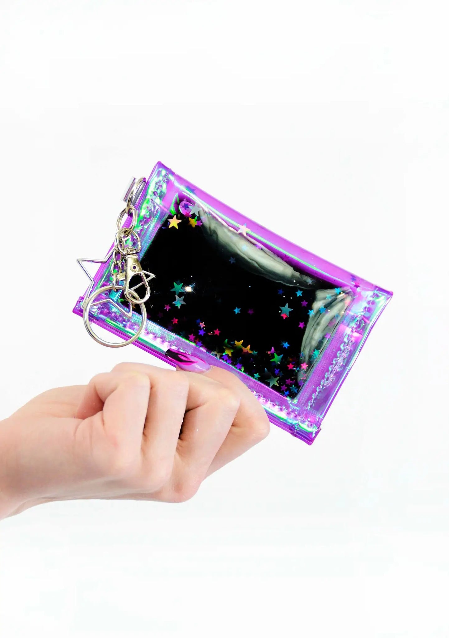 Rectangular wallet made of silver and iridescent purple vinyl filled with liquid glitter in purple, blue, black, and silver holographic star shaped glitter. It has a silver metal star shaped key ring. Shown held 
