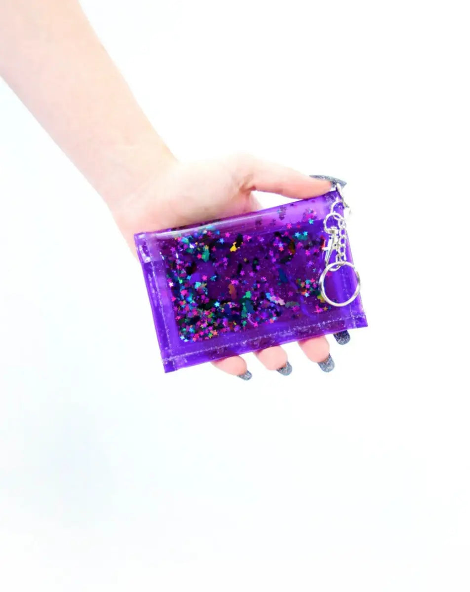 A rectangular wallet made of sparkly purple vinyl filled with clear liquid and black bat purple & black star holographic glitter. Shown held