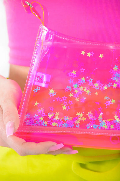A trapezoid shaped mini purse made of neon pink vinyl with a matching arm strap. The body of the purse has liquid glitter floating in it in purple, green, blue, and pink Star shapes. Shown in close up of glitter 