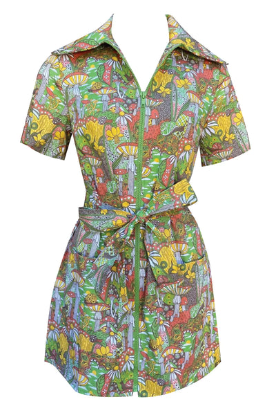 A short sleeved mini dress with an exaggerated pointed collar and green plastic zipper down the front. It has a psychedelic pattern with motifs including star spotted mushrooms, daffodils, paisley, snails, and pinwheels- in shades of yellow, red, green, and black. Shown from front zipped with sash belt