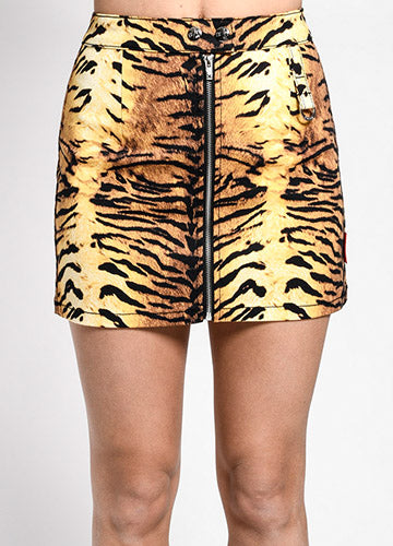 Cotton stretch twill mini skirt in an all-over black, orange, and yellow tiger print. It has a double snap closure at the waistband and a heavy duty silver metal zipper down the front. There is a matching fabric tab with silver metal D-ring on the left hip of the front and back of the skirt. Seen on a model from the front