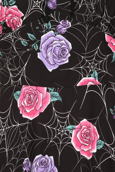 Close up shot of dress pattern. Rayon knit fabric stylized white spiderweb with purple and pink rose pattern on a black background