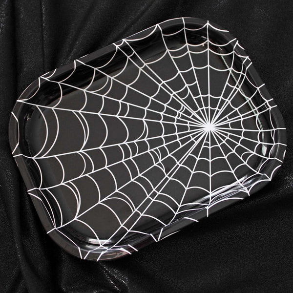 Rectangular tin tray with a wide lip. It has an all-over white spiderweb design on a black background. Shown from above on a black velvet background 
