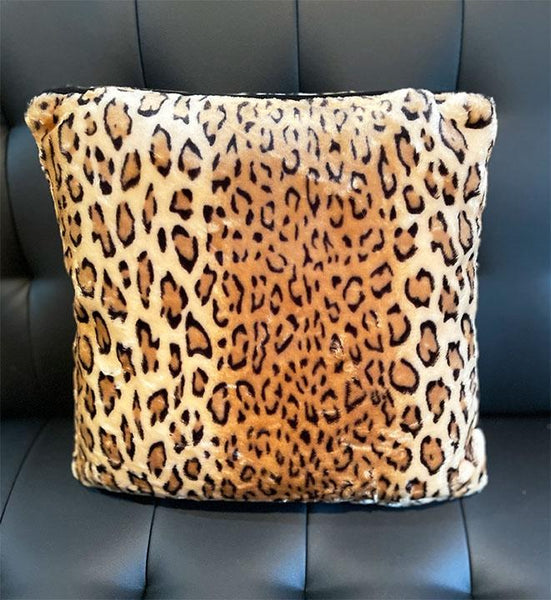 leopard print velvet square pillow with black velvet piping shown on black leather couch 