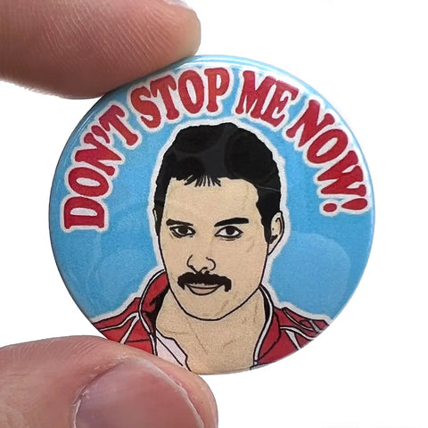 Stylized portrait of Freddie Mercury with the caption “DON’T STOP ME NOW!” in red above on a 1 1/2” round pinback button