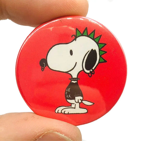 A Snoopy-like cartoon with a green Mohawk and piercings on a red background on a 1 1/2” pinback button 