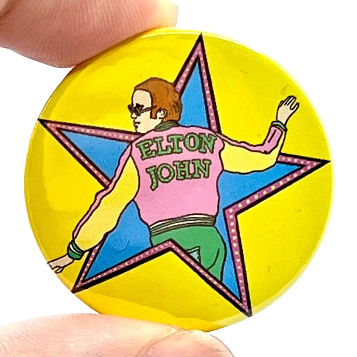 neon colored illustration of Elton John from the cover of the album ﻿Goodbye Yellow Brick Road on a chartreuse background on a 1 1/2” round pinback button