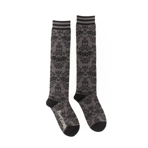 Knee socks with a monochromatic damask pattern of flying bats. Striped grey and black bands at the top of each sock and solid black toes and heels. Shown from the side