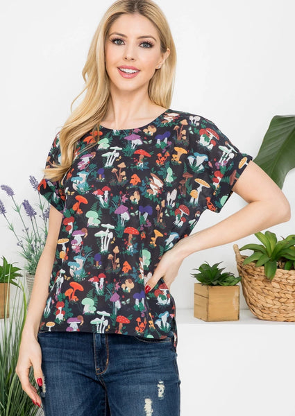 Model wearing black background allover assorted woodsy mushrooms print relaxed fit crew neckline top featuring keyhole button closure at the nape, cuff detail short sleeves, curved bottom hem. Shown with one hand on hip