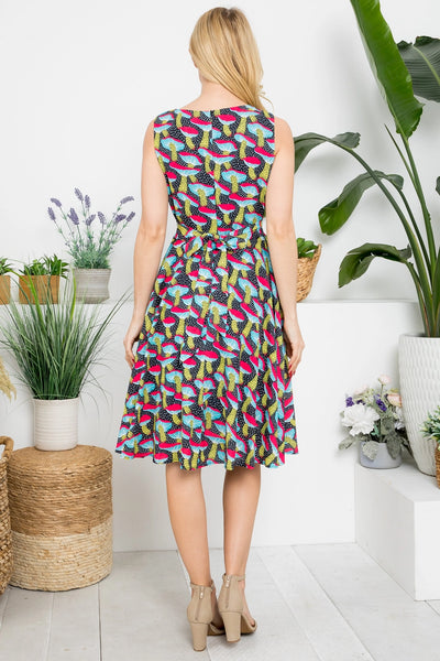 Model wearing black and white dotted background with allover pink, blue, yellow, and red mushroom print sleeveless fit & flare dress with darted bust, self tie belt and pockets. Shown from behind